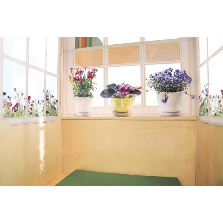 Inside view of the Whitney Brothers Nature View Window Seat, where potted flowers seen through bright window panels create a calm corner above the green cushioned seat