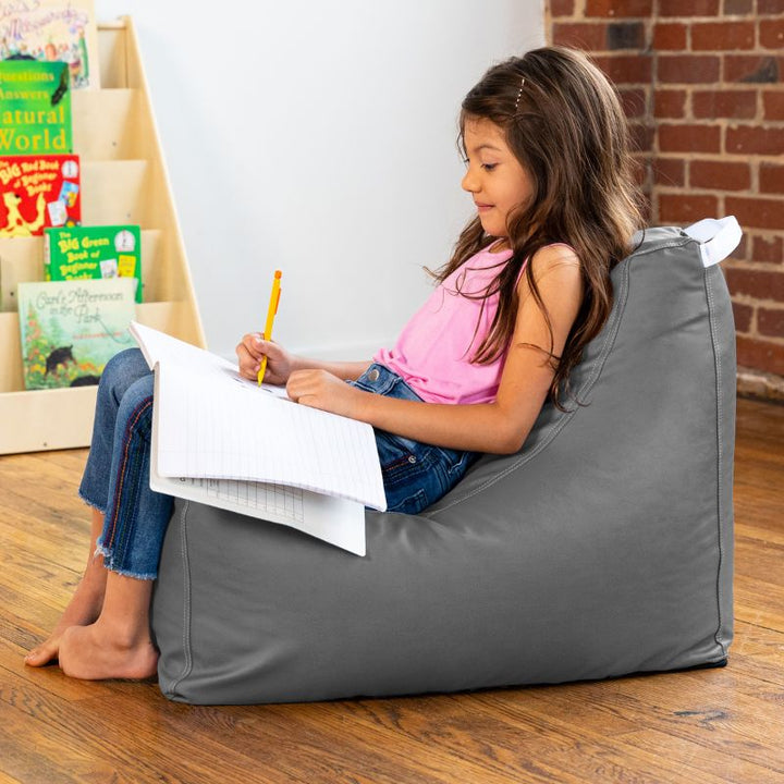 Child doing schoolwork on the Jaxx Pezzi classroom bean bag chair in charcoal vinyl with a carry handle