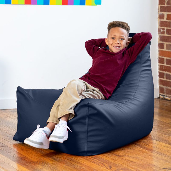 Child lounging on the Jaxx Pezzi classroom bean bag chair in navy blue vinyl, comfortable seating for quiet breaks