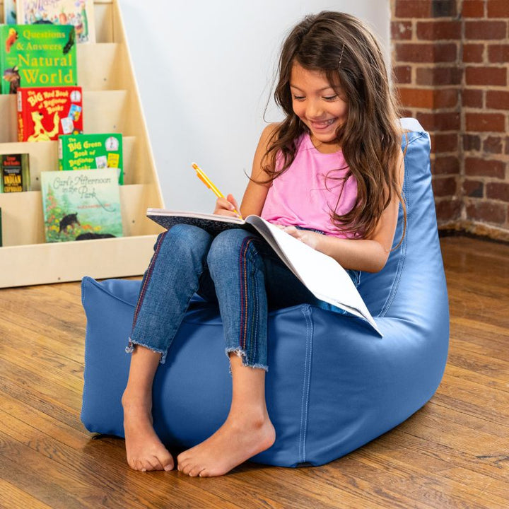 Child writing in a notebook on the Jaxx Pezzi classroom bean bag chair in royal blue vinyl in a school library corner