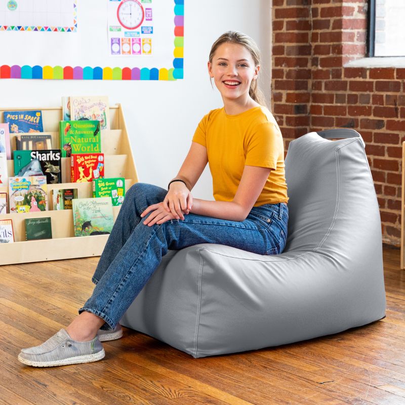 Student seated on the Jaxx Pezzi classroom bean bag chair in submarine grey vinyl in a school library reading nook