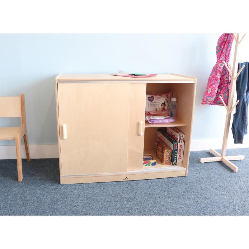 Whitney Brothers Sliding Doors Storage Cabinet with one door open, a classroom storage cabinet holding care supplies on the shelf and board games below