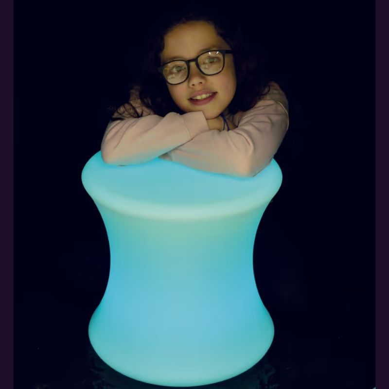 Child resting on the TFH Colour Morphing Stool glowing blue, a portable sensory light seat for calm corners