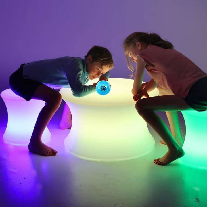 Two children exploring a light-up sensory ball beside TFH Colour Morphing Stools glowing purple and green