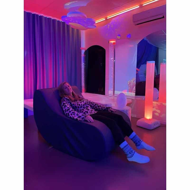 A child relaxing in a sensory room lit by the TFH Genie Colour Wash Kit's soft purple and pink interactive lighting