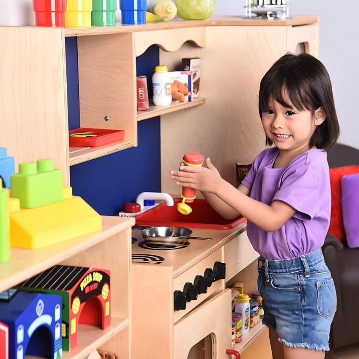 Close-up view of a child playing at the Constructive Playthings Five-In-One Kitchen, showing the turning stove knobs and acrylic oven panel detail on this classroom play kitchen