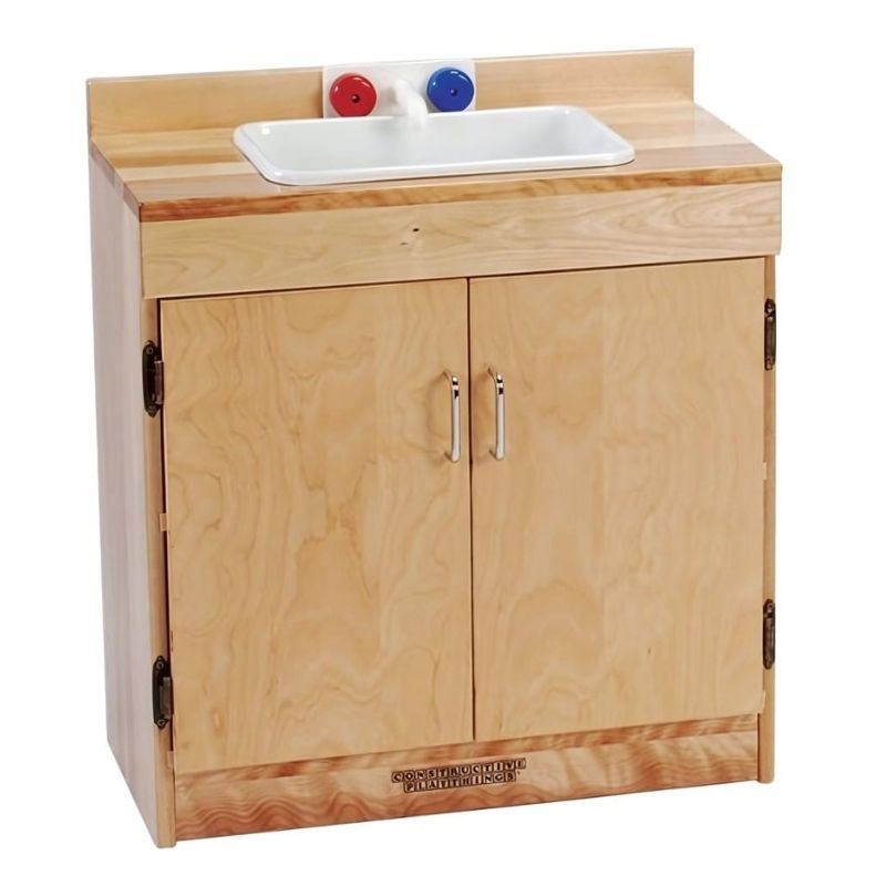 Constructive Playthings Town & Country Kitchen sink cabinet in solid maple with chrome pulls on magnetic-closing doors and laminated shelves, part of the 4-piece classroom play kitchen