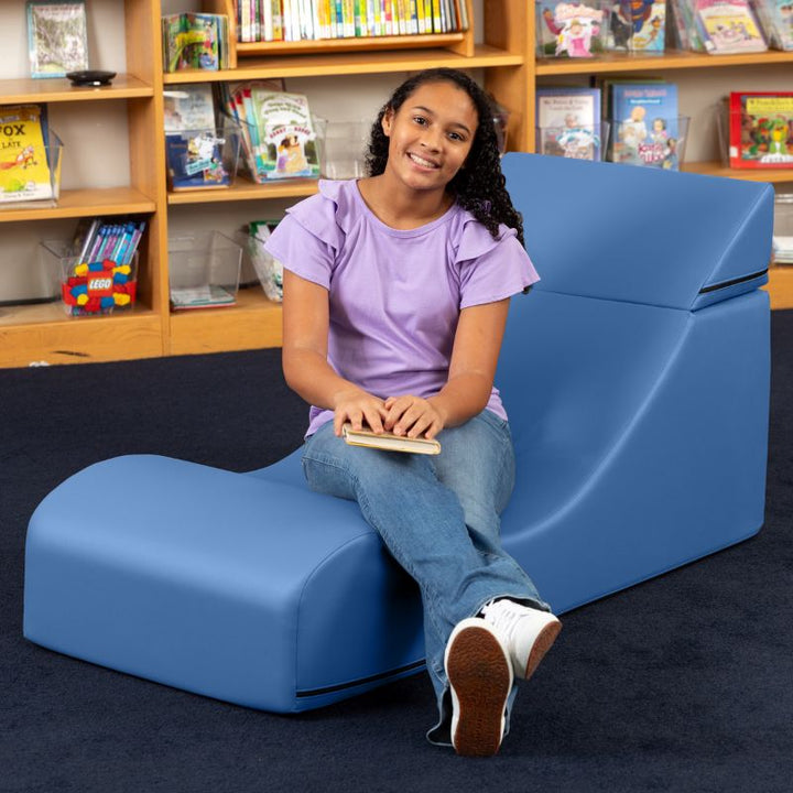 A student seated in the Jaxx Flexx convertible foam chair in blue vinyl, a sensory foam chair for school libraries