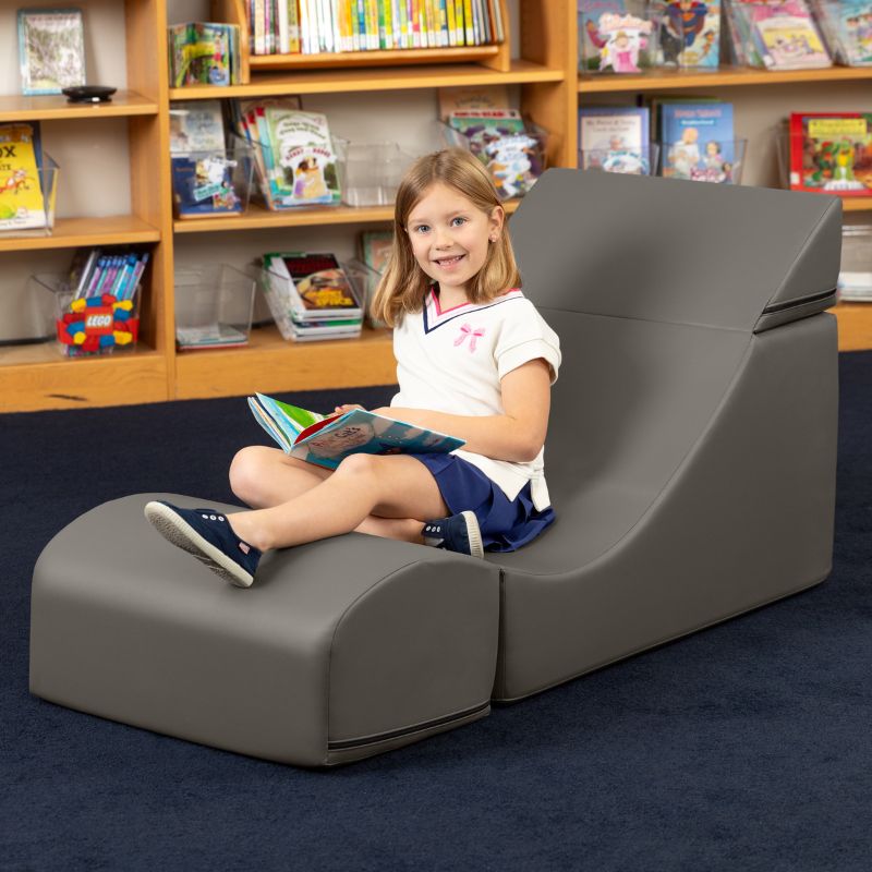 A child reading while seated in the Jaxx Flexx convertible foam chair in charcoal vinyl in a school library setting