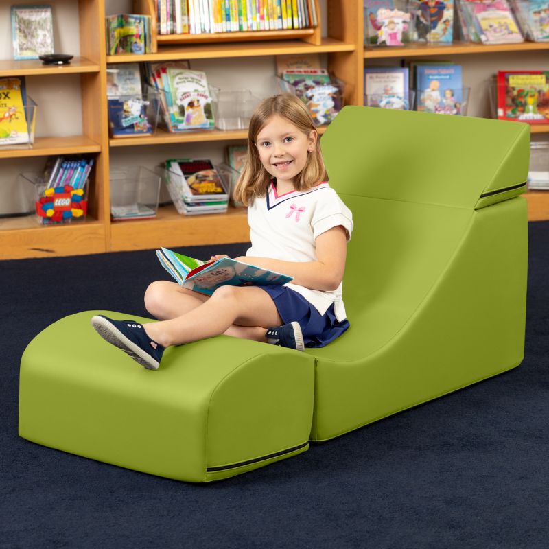 A child reading while seated in the Jaxx Flexx convertible foam chair in green vinyl, a sensory foam chair for classroom reading nooks