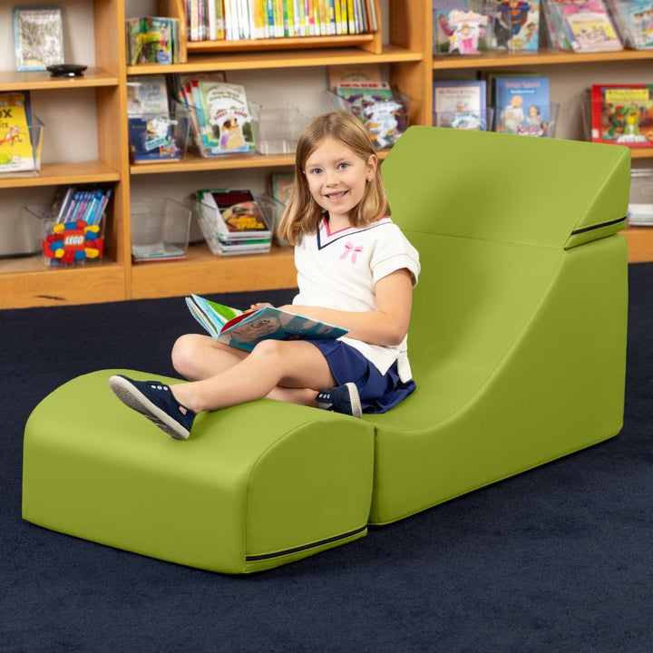 A child reading while seated in the Jaxx Flexx convertible foam chair in green vinyl, a sensory foam chair for classroom reading nooks