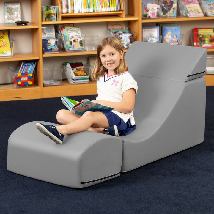 A child reading while seated in the Jaxx Flexx convertible foam chair in grey vinyl in a school library reading nook