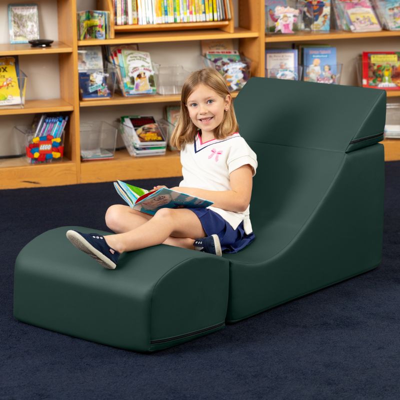 A child reading while seated in the Jaxx Flexx convertible foam chair in deep sequoia green vinyl in a school library setting