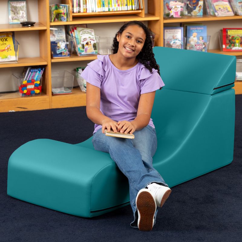 A student seated in the Jaxx Flexx convertible foam chair in teal vinyl, a sensory foam chair for school reading nooks