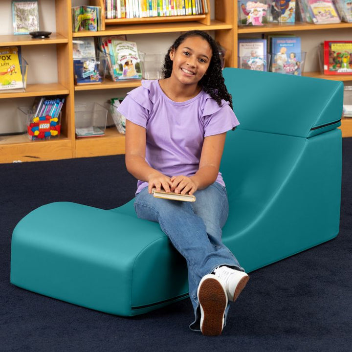 A student seated in the Jaxx Flexx convertible foam chair in teal vinyl, a sensory foam chair for school reading nooks