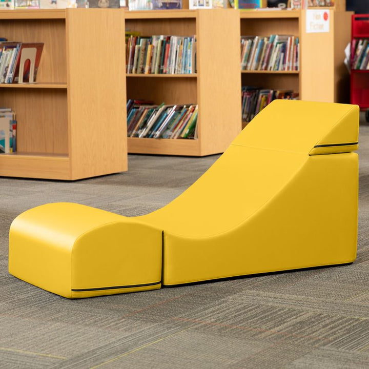 Jaxx Flexx convertible foam chair in yellow vinyl staged in a school library reading corner