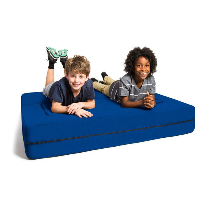 Two kids relaxing on the Jaxx Zipline flip sofa in blue, shown flattened out as a kids lounging bed