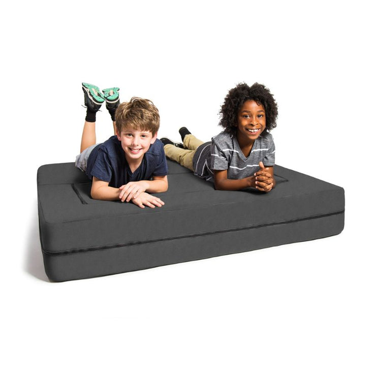 Two kids lying on the Jaxx Zipline convertible kids sofa in grey, unfolded flat for lounging or reading