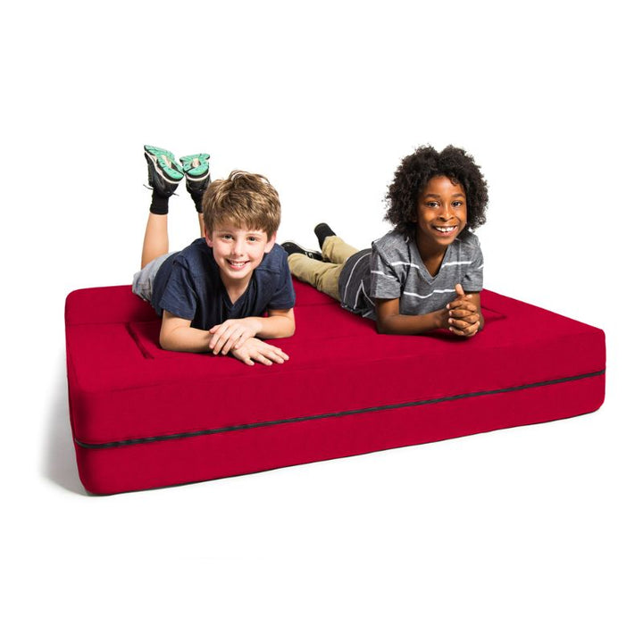 Two kids lying on the Jaxx Zipline convertible kids sofa in red, folded flat into its bed configuration