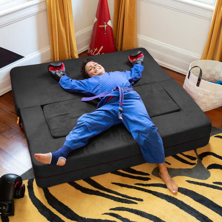 A boy relaxing on the Jaxx Zipline flip sofa in black, shown flat as a lounging bed in a bedroom