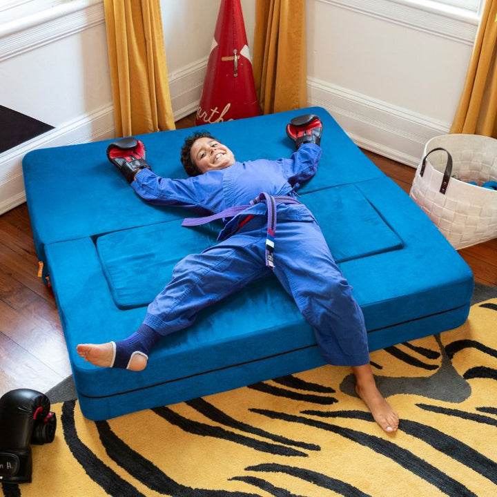 A boy relaxing on the Jaxx Zipline flip sofa in teal, flattened into a lounging bed in a bedroom setting