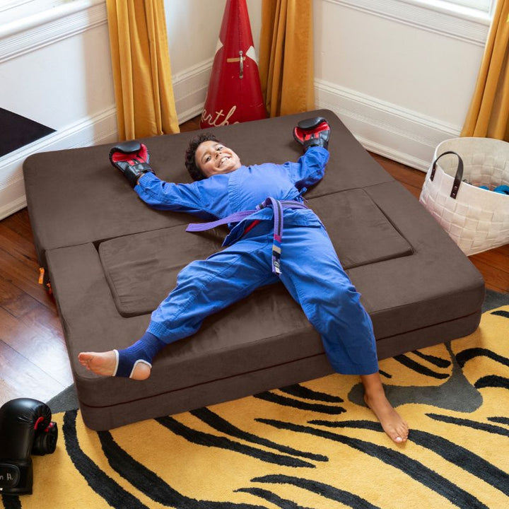 A boy relaxing on the Jaxx Zipline flip sofa in brown, unfolded flat into a kids lounging bed