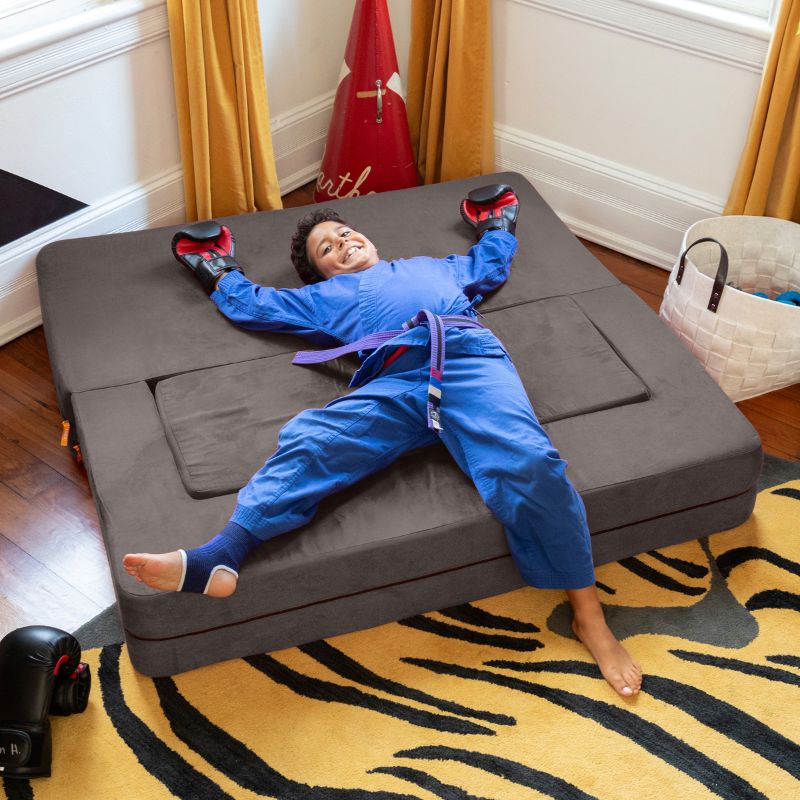 A boy lying on the Jaxx Zipline convertible kids sofa in charcoal, flattened into its bed configuration
