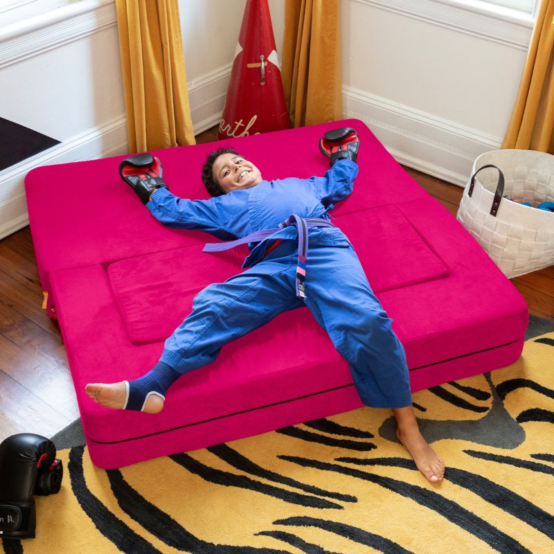 A boy lying on the Jaxx Zipline convertible kids sofa in pink, unfolded flat into its bed configuration in a bedroom
