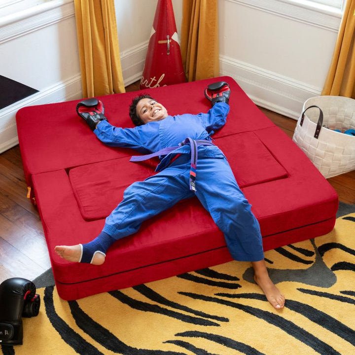 A boy lying on the Jaxx Zipline convertible kids sofa in red, shown flat in its bed configuration at home