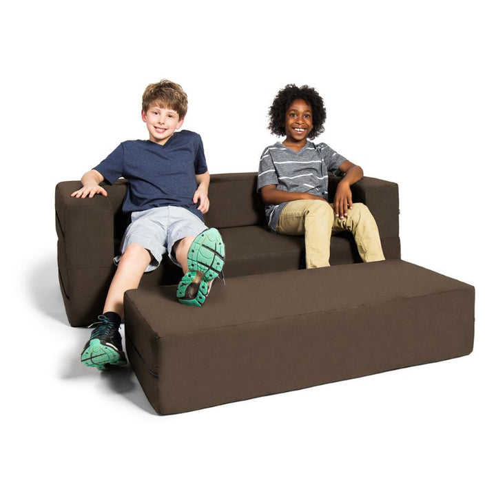 Two kids relaxing on the Jaxx Zipline convertible kids sofa in brown, with the ottoman positioned as a footrest