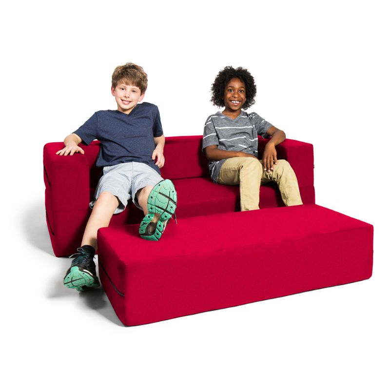 Two kids sitting on the Jaxx Zipline convertible kids sofa and ottoman in red, showing scale for a library or reading corner setup