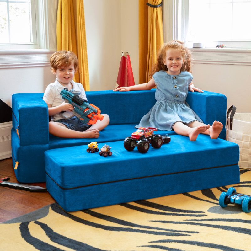 Two kids playing with toy trucks on the Jaxx Zipline flip sofa and ottoman in blue
