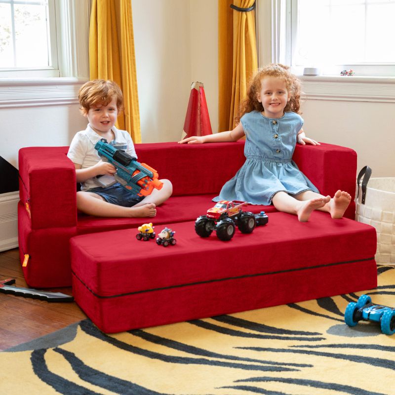 Two kids sitting on the Jaxx Zipline convertible kids sofa in red, with toys spread across the ottoman