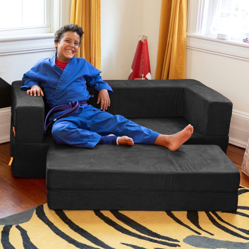 A boy relaxing on the Jaxx Zipline convertible kids sofa in black, shown styled in a bedroom setting