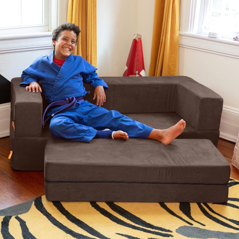 A boy relaxing on the Jaxx Zipline convertible kids sofa in brown, shown in a bedroom lifestyle setting