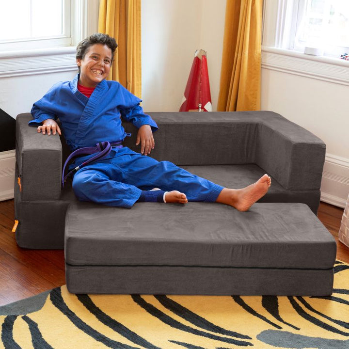 A boy sitting on the Jaxx Zipline flip sofa and ottoman in charcoal, styled in a real bedroom