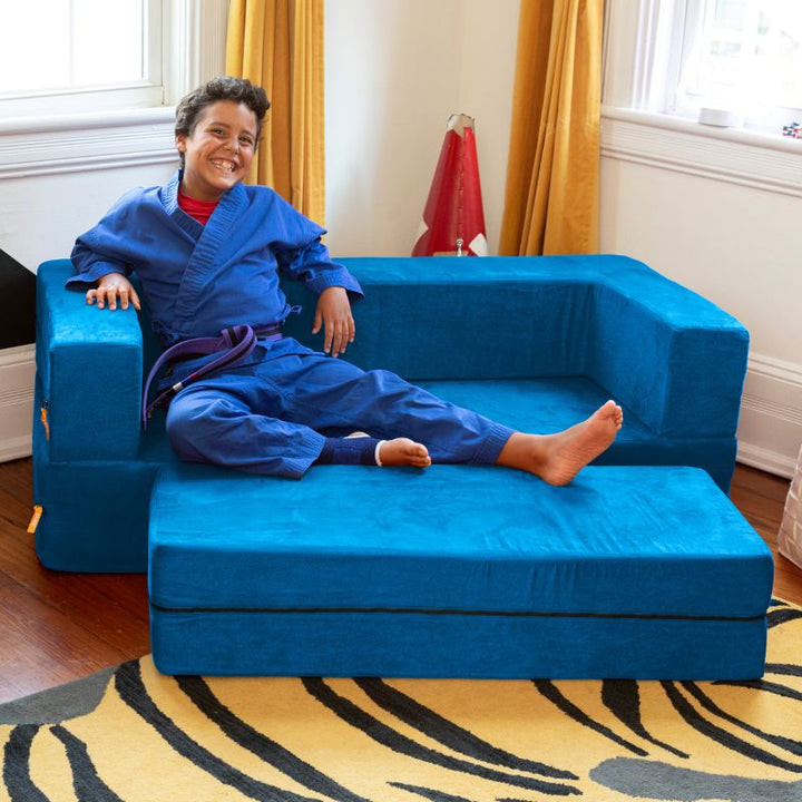A boy relaxing on the Jaxx Zipline flip sofa in teal, shown styled in a real bedroom setting