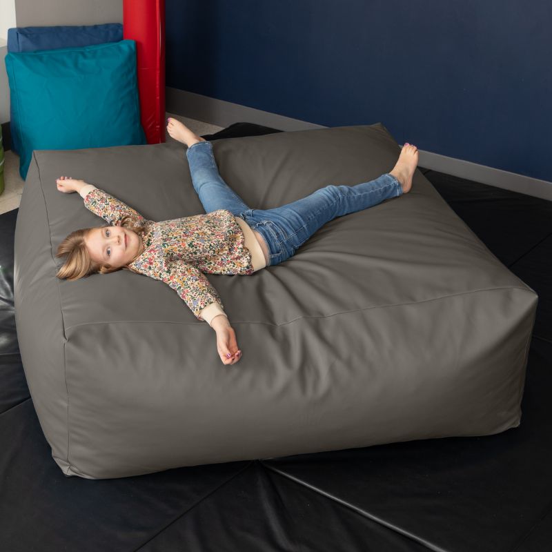 A young girl relaxes on the charcoal Jaxx Crash Mat 48in in a school sensory room, showing the crash mat's full-body landing surface