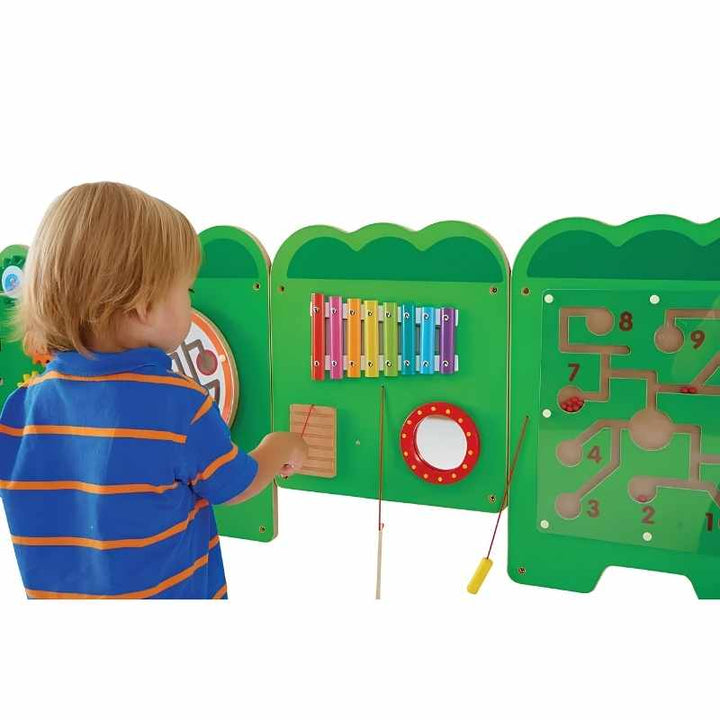 A toddler reaches for the xylophone and mirror section of the TFH Crocodile Activity Wall Panel, a hands-on sensory wall panel for classrooms and homes