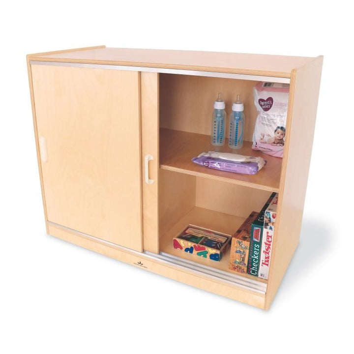 Whitney Brothers Sliding Doors Storage Cabinet open to reveal a deep interior shelf with baby bottles, wipes, puzzles and games for daycare storage