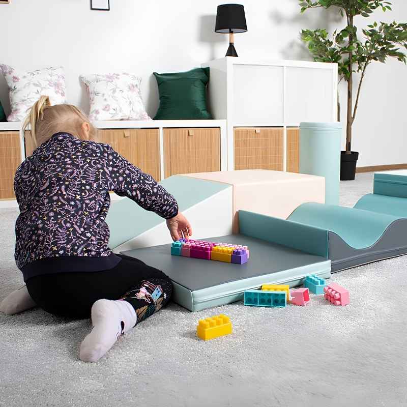 Girl sitting beside the IGLU Discoverer Soft Play Set in Pastel Turquoise, playing with building blocks