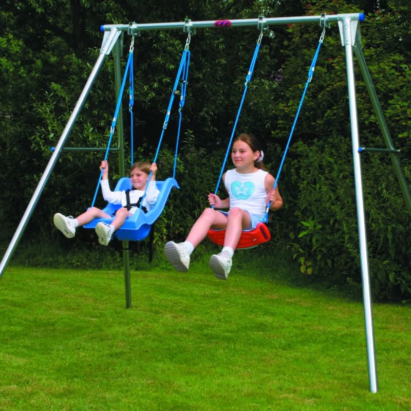 Two children swinging side by side on a TFH Double Swing Frame, one in a full support seat and one on a standard seat, in a backyard sensory swing set up