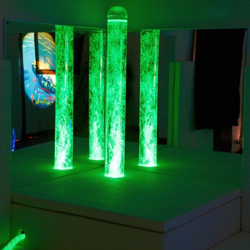 Experia Bubble Tube Mirrors corner installation in green light, demonstrating how the corner-mounted acrylic pair multiplies the bubble tube colour across the sensory room