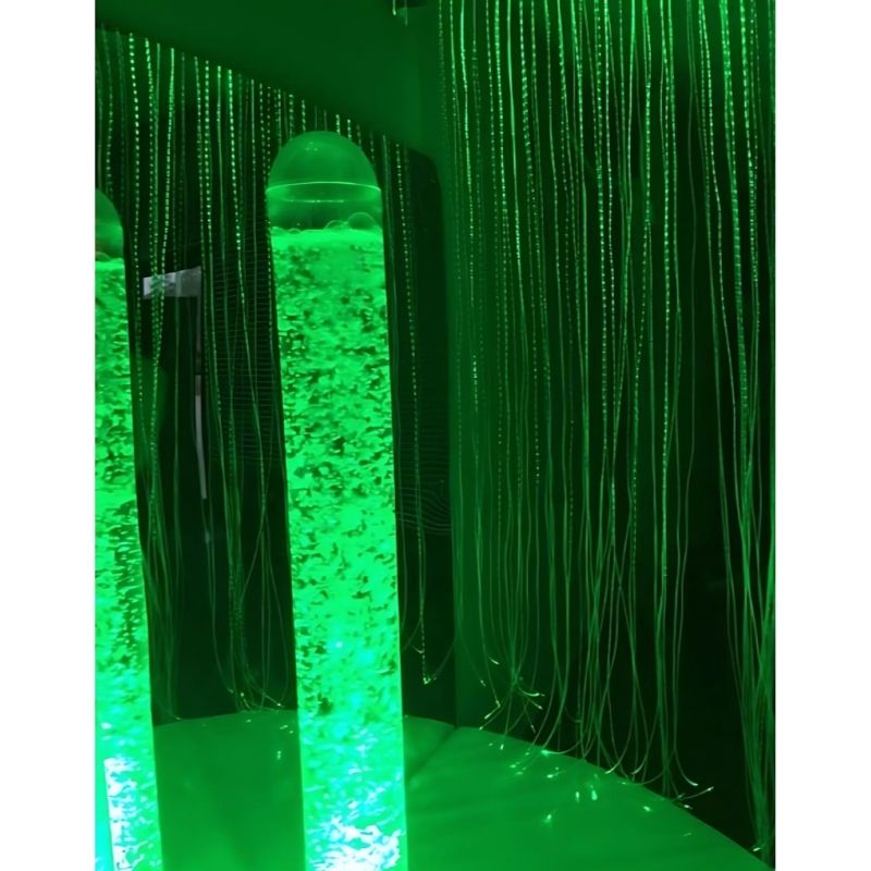 Close-up of the Experia Calming Sensory Cocoon LED bubble tube glowing in green light, showing the self-colour cycling calming bubble tube at the centre of the sensory cocoon environment
