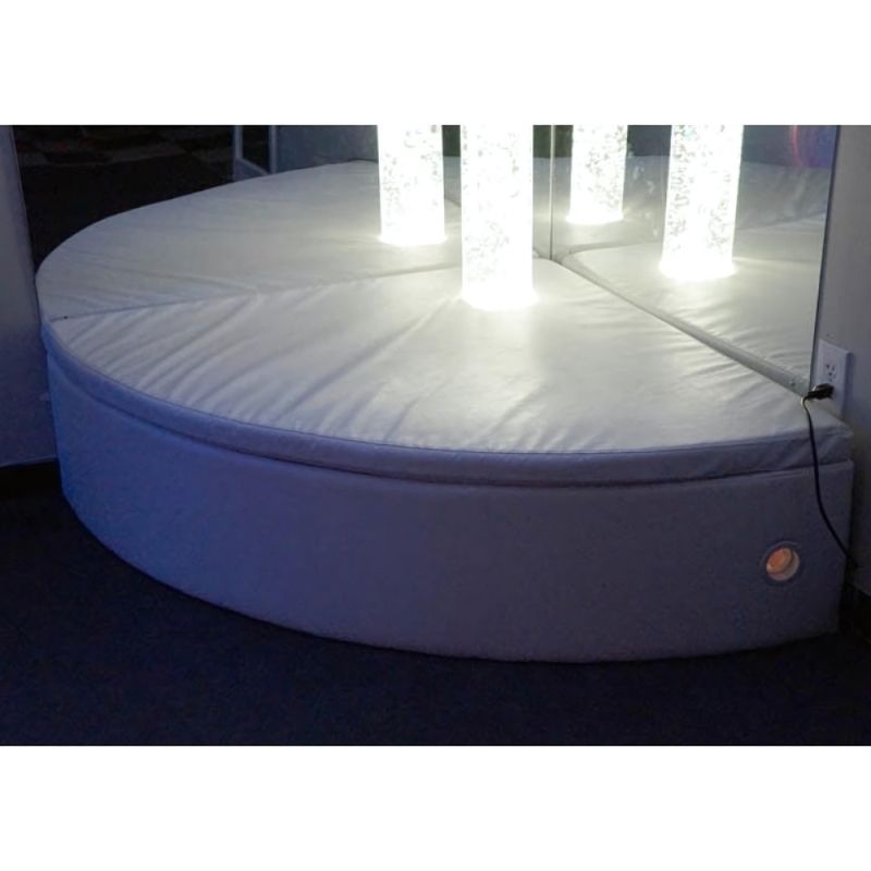 Experia Curved Bubble Tube Platform in white shown in a sensory room corner with bubble tube glowing, demonstrating the curved seating platform for 6-inch diameter bubble tubes