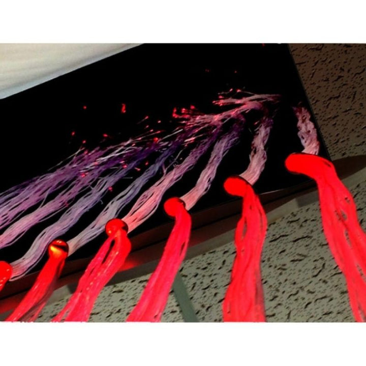 Close-up of the Experia Fibre Optic Raincloud in red light showing the 150 safe-to-touch colour-changing fibre optic raindrop strands that users can walk through and feel