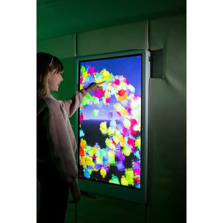 Child laughing while engaging with the Experia Intelli Panel Particle interactive sensory wall panel in a green-lit room