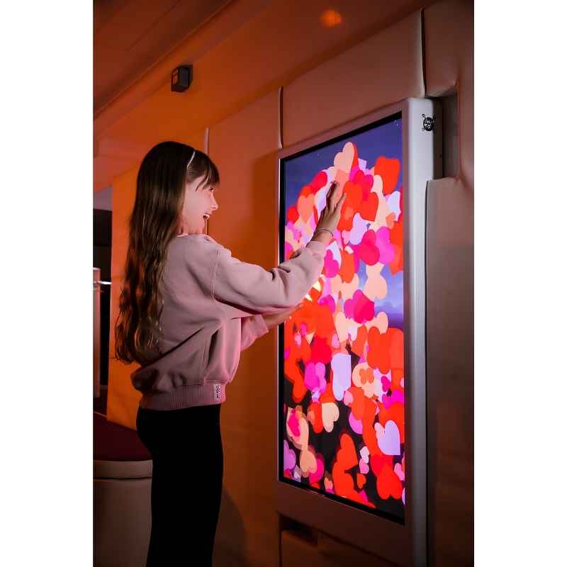Side view of a child engaging with the Experia Intelli Panel Particle touchscreen sensory wall panel in an orange-lit room
