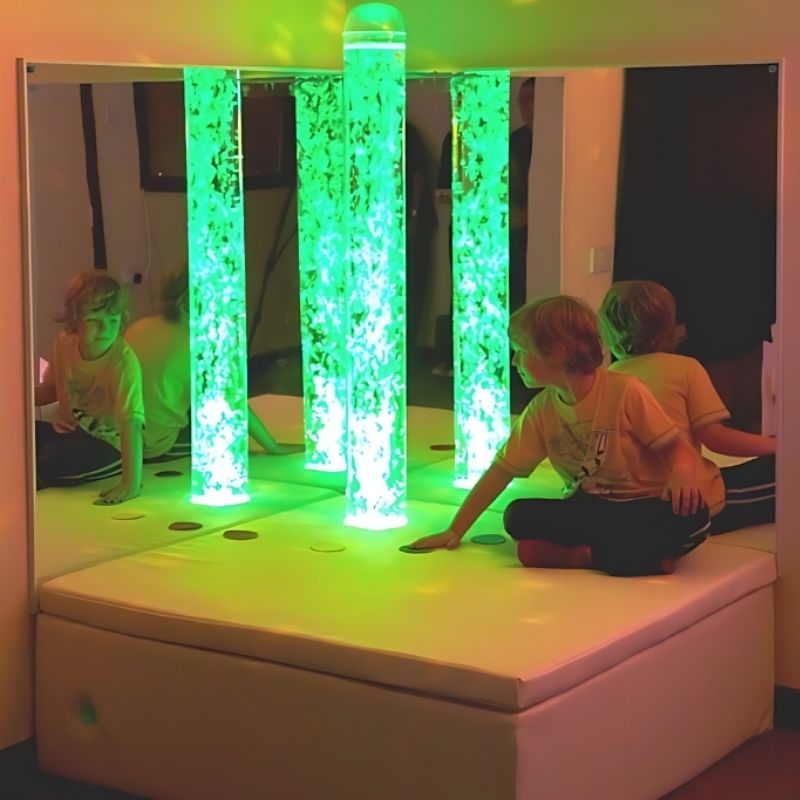 Child actively engaging with the Experia Interactive Bubble Tube Corner platform switches in green light, demonstrating cause-and-effect colour control of the sensory bubble tube