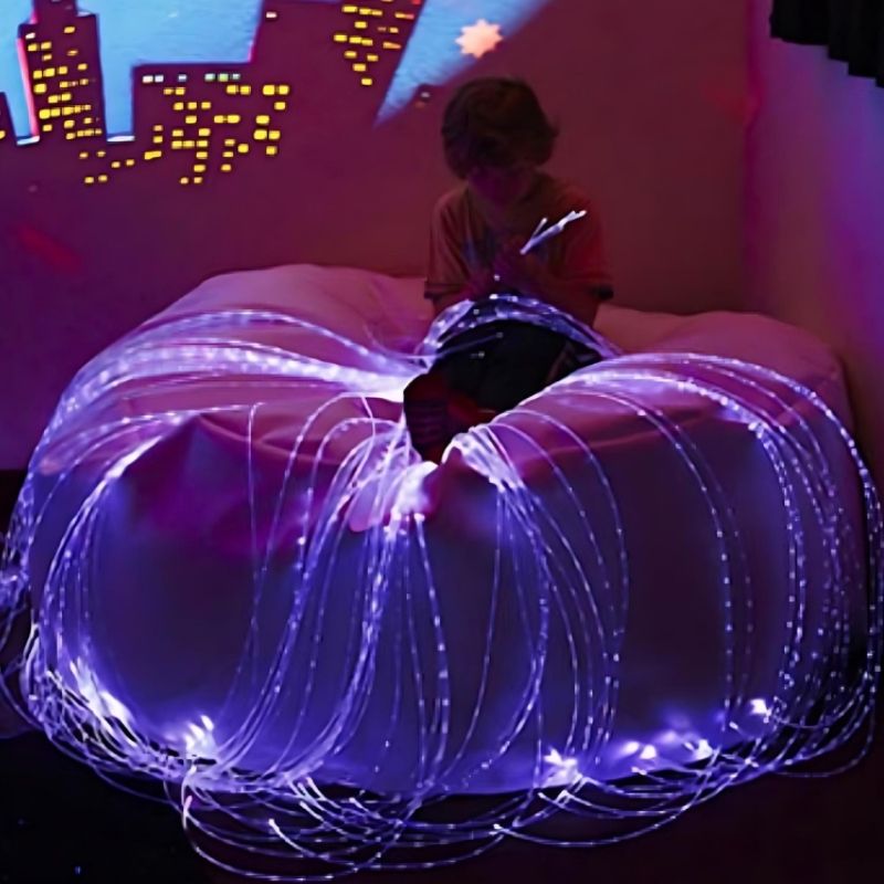 Child actively holding and exploring the Experia LED Fibre Optic Softie in purple light while seated in the beanbag, demonstrating the lap-safe tactile fibre optic sensory experience